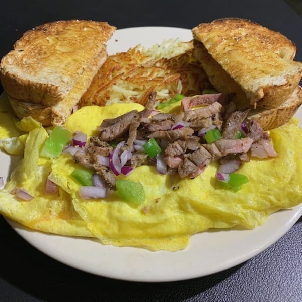 A diner breakfast with a steak omelet topped with onions and peppers, hash browns, and toast.