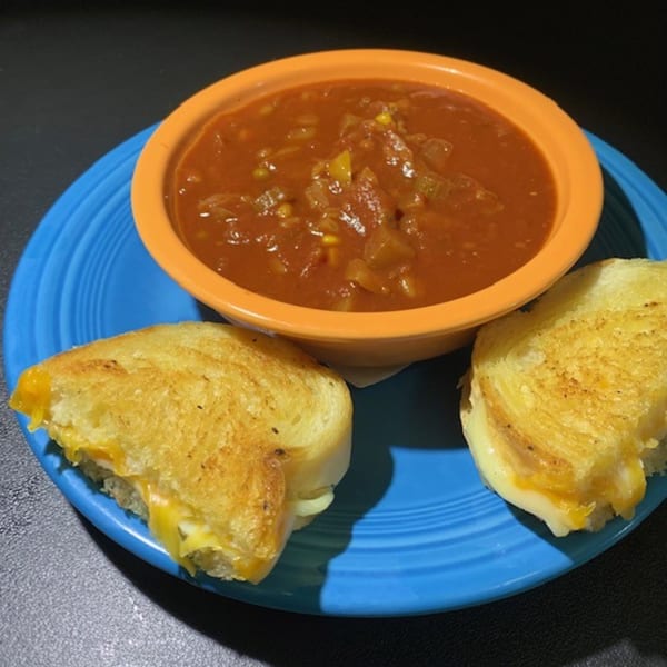 A diner-style meal of tomato soup with vegetables and two grilled cheese sandwich halves on a blue plate.