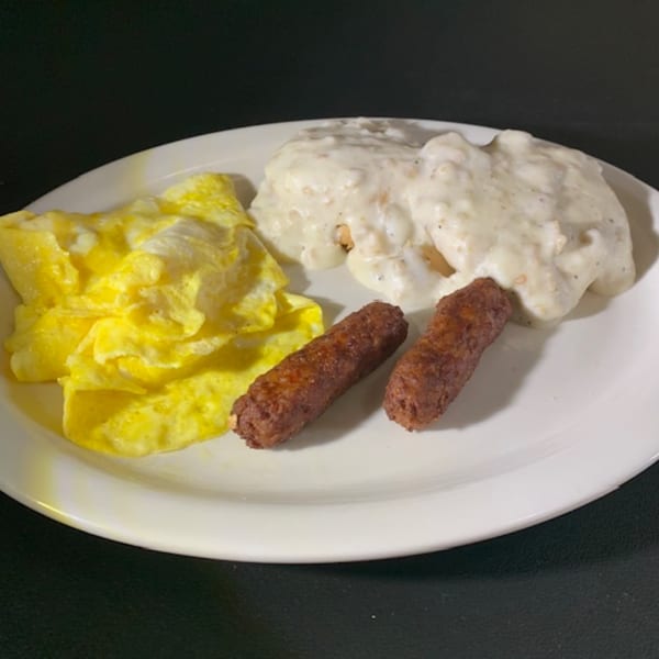 A diner breakfast plate with scrambled eggs, two sausage links, and biscuits with gravy.