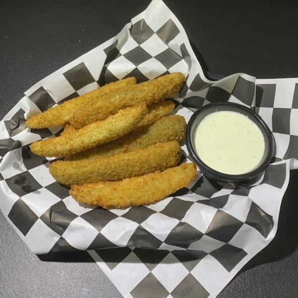 Golden-brown fried pickles and a side of creamy dipping sauce in a diner basket.